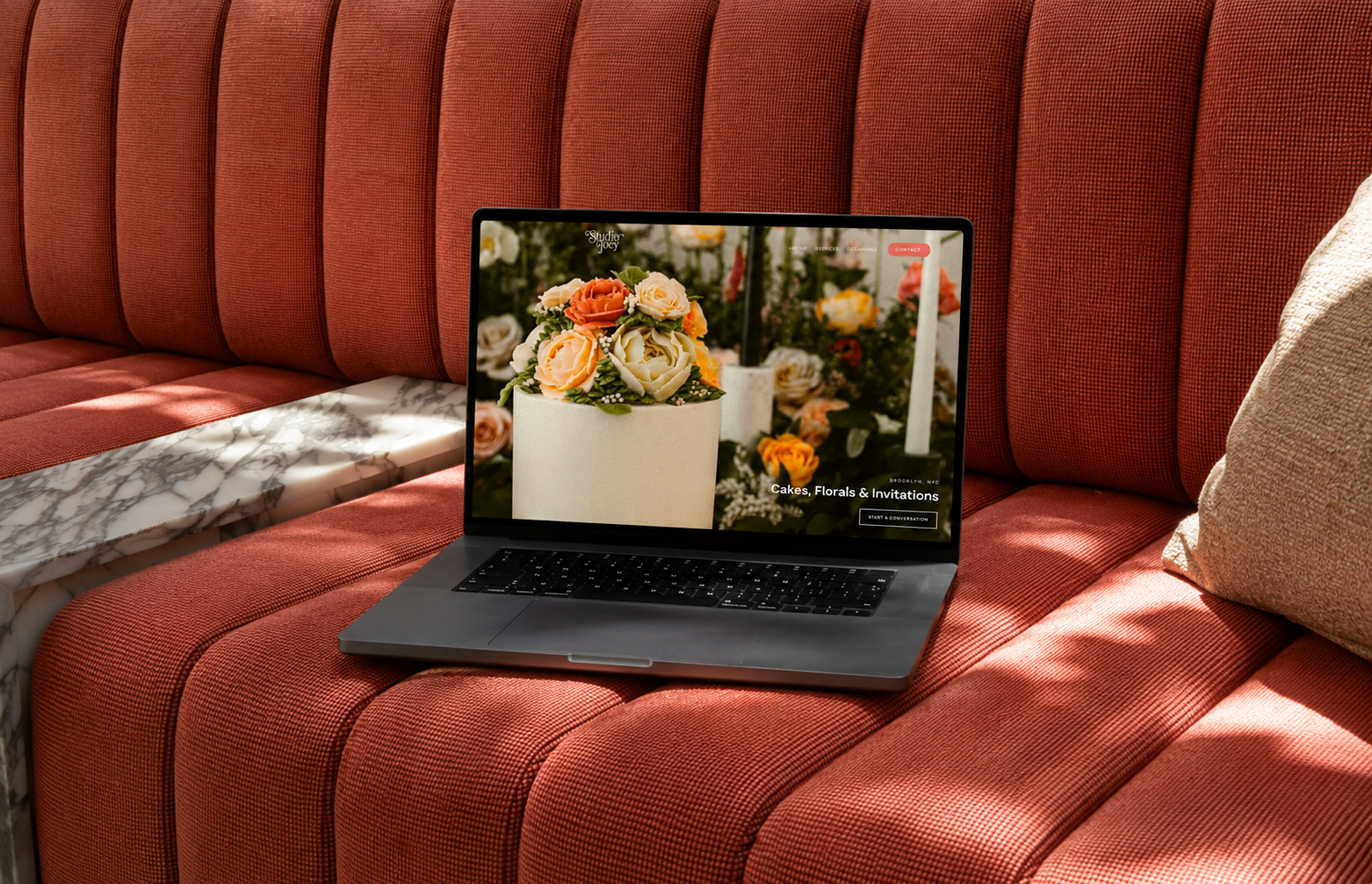 Studio Joey website displayed on MacBook laptop on terracotta sofa